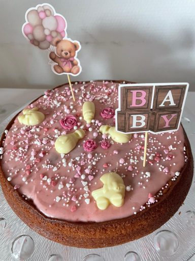 Feestelijke babytaart met roze glazuur, confetti en decoraties van teddyberen en ballonnen.
